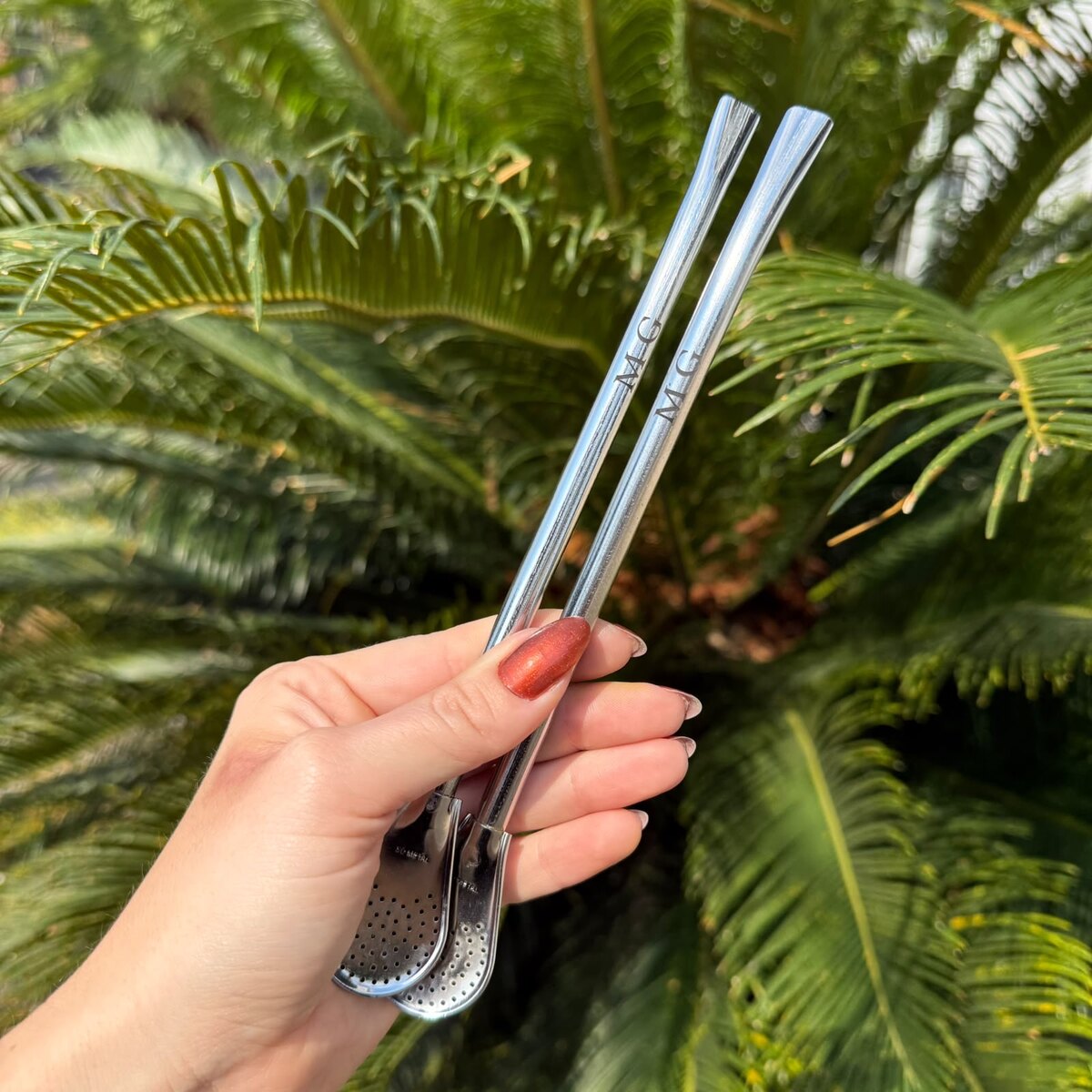 Mão segurando bombas de inox gravadas com iniciais — personalização FEITIO
